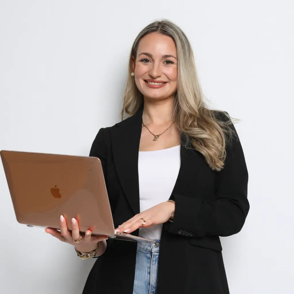 Alina hält einen Laptop in der Hand und schaut konzentriert nach vorne.